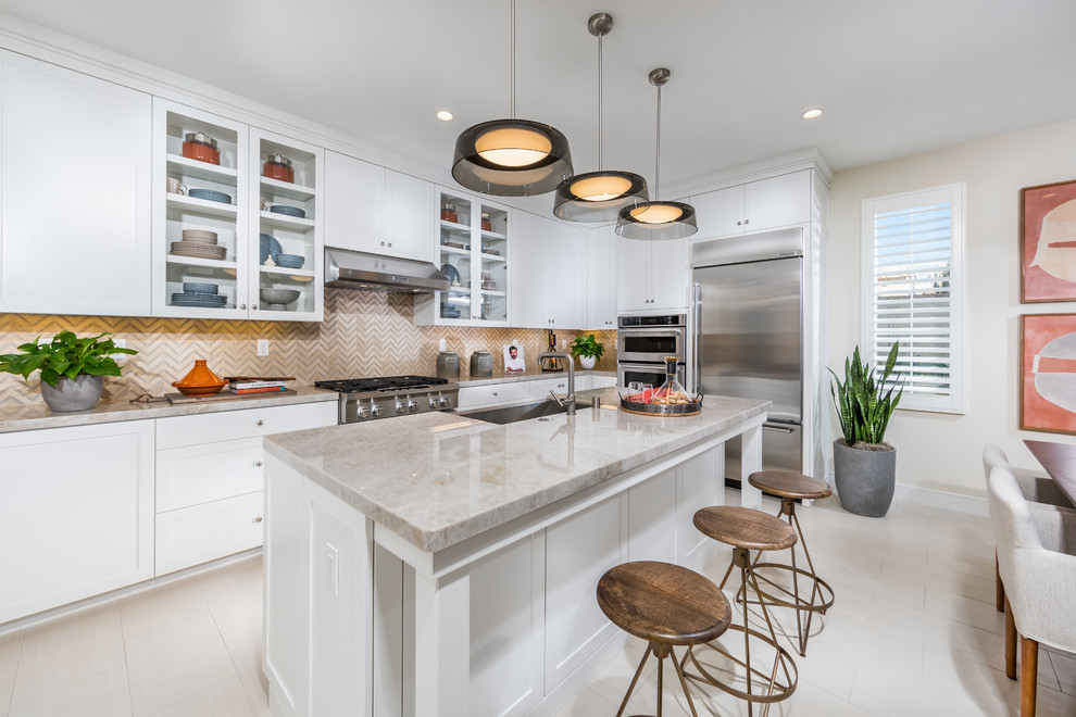 Inspiration for a classic l-shaped kitchen/diner in Orange County with a belfast sink, shaker cabinets, white cabinets, beige splashback, stainless steel appliances, an island and beige worktops.