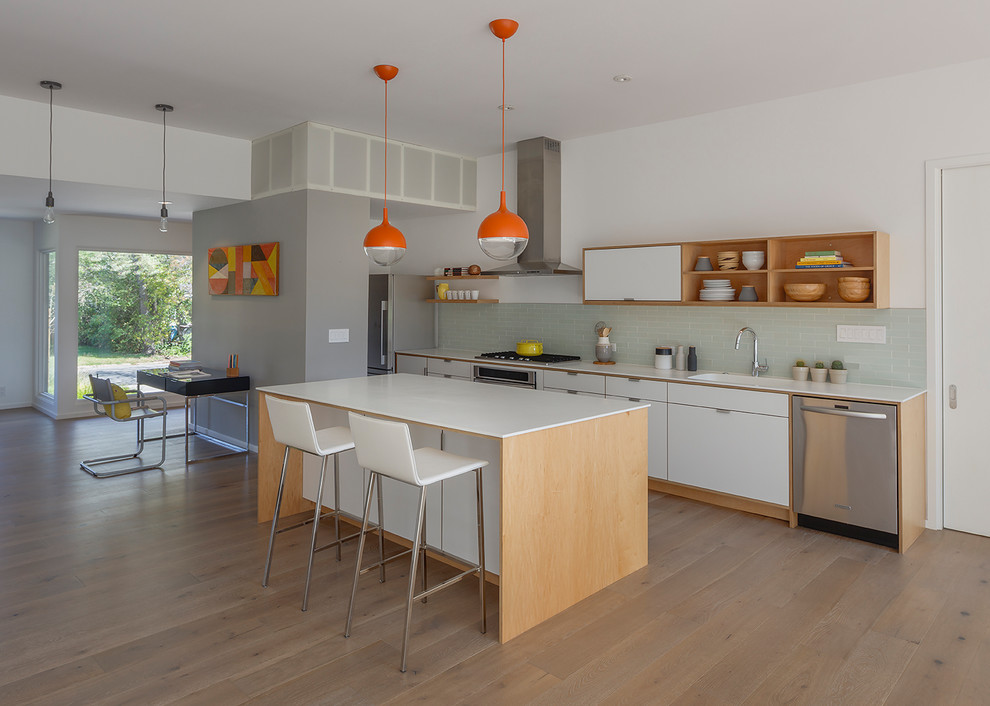 Example of a mid-century modern single-wall medium tone wood floor and brown floor open concept kitchen design in San Francisco with an undermount sink, flat-panel cabinets, white cabinets, solid surface countertops, green backsplash, subway tile backsplash, stainless steel appliances and an island