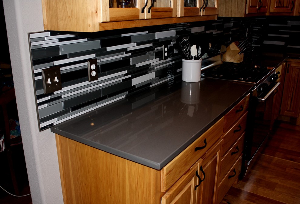 Modelo de cocina actual con encimera de cuarzo compacto, salpicadero negro, salpicadero de azulejos de vidrio y una isla