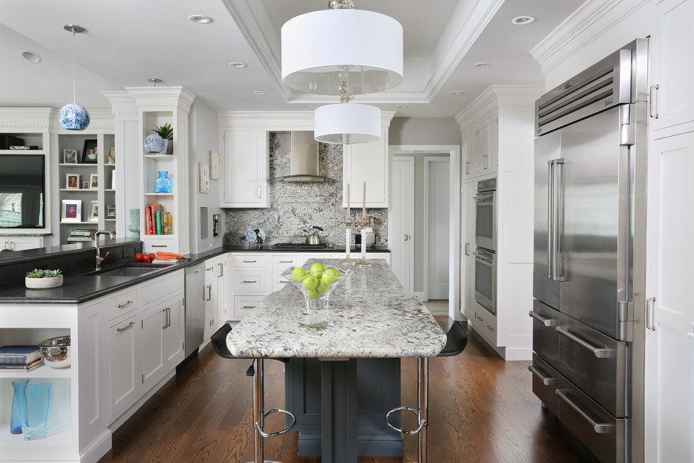Exempel på ett mellanstort klassiskt kök, med en undermonterad diskho, luckor med infälld panel, vita skåp, granitbänkskiva, grått stänkskydd, stänkskydd i sten, rostfria vitvaror, mörkt trägolv och en köksö