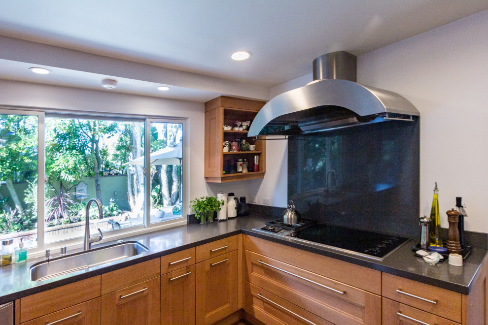 This is an example of a medium sized classic u-shaped kitchen/diner in Orange County with a single-bowl sink, recessed-panel cabinets, beige cabinets, engineered stone countertops, black splashback, engineered quartz splashback, stainless steel appliances, cork flooring, an island, brown floors and black worktops.