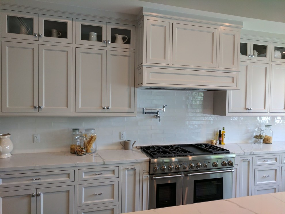 Maritim inredning av ett stort vit vitt kök, med en undermonterad diskho, luckor med infälld panel, vita skåp, bänkskiva i kvarts, vitt stänkskydd, stänkskydd i sten, rostfria vitvaror, klinkergolv i porslin, en köksö och grått golv