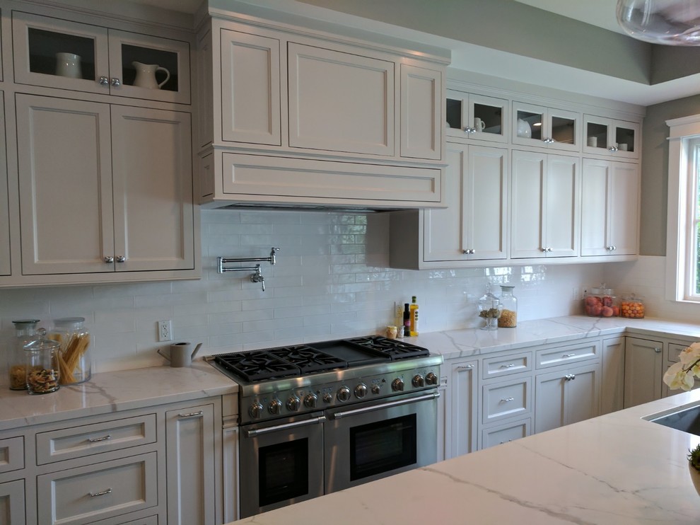 Photo of a large nautical u-shaped kitchen/diner in Orange County with a submerged sink, recessed-panel cabinets, white cabinets, engineered stone countertops, white splashback, stone slab splashback, stainless steel appliances, porcelain flooring, an island, grey floors, white worktops and exposed beams.