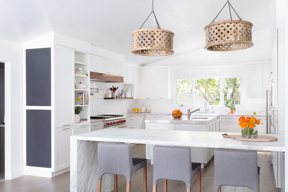 Beach style kitchen in Los Angeles with a single-bowl sink, shaker cabinets, white cabinets, white splashback, stainless steel appliances, light hardwood flooring and multiple islands.