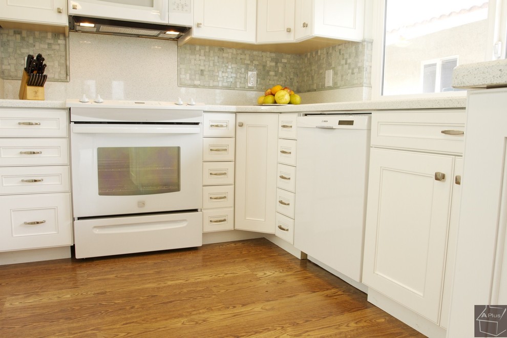 Idéer för att renovera ett mellanstort vintage kök, med en nedsänkt diskho, luckor med infälld panel, vita skåp, bänkskiva i kvarts, grönt stänkskydd, stänkskydd i mosaik, vita vitvaror, ljust trägolv och en halv köksö