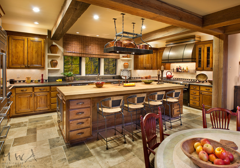 Foto på ett stort rustikt brun kök, med en undermonterad diskho, luckor med profilerade fronter, skåp i mellenmörkt trä, träbänkskiva, rostfria vitvaror, en köksö, svart stänkskydd, skiffergolv och flerfärgat golv