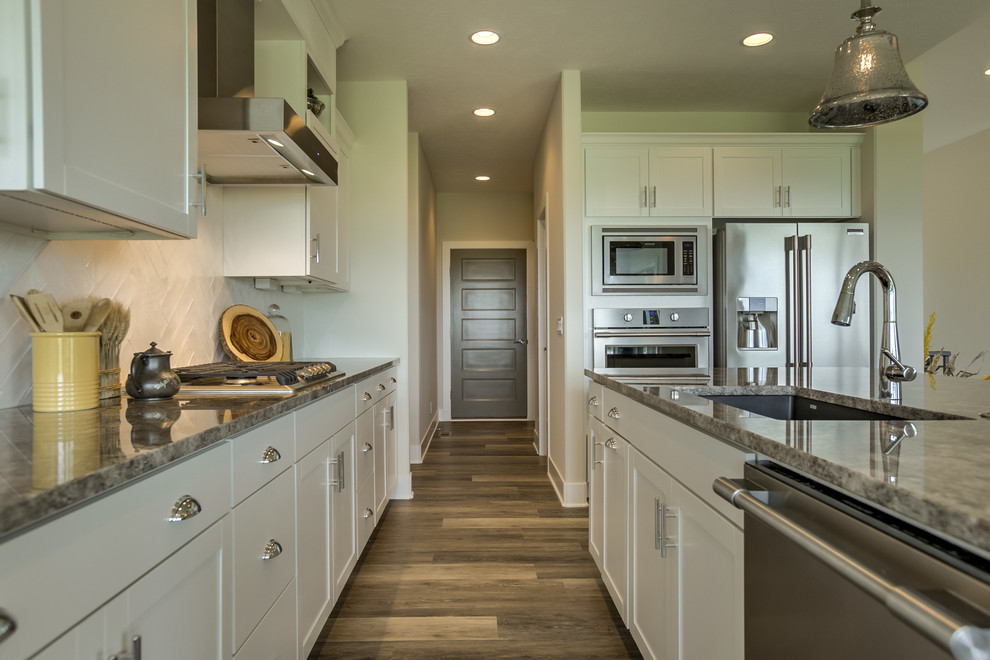 Inspiration for a transitional open concept kitchen remodel in Omaha with an undermount sink, shaker cabinets, white cabinets, granite countertops, white backsplash, stainless steel appliances and an island
