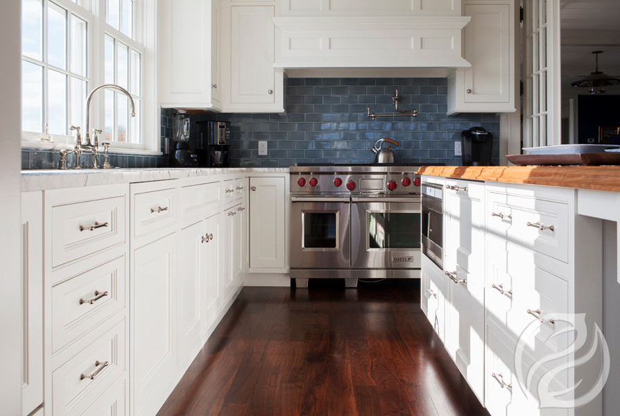Klassische Küche in L-Form mit weißen Schränken, Küchenrückwand in Blau, Rückwand aus Keramikfliesen, Küchengeräten aus Edelstahl, braunem Holzboden, Kücheninsel und Kassettenfronten in Boston