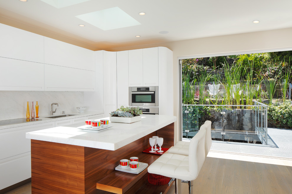 Ejemplo de cocina contemporánea con armarios con paneles lisos, puertas de armario blancas, salpicadero blanco y electrodomésticos de acero inoxidable