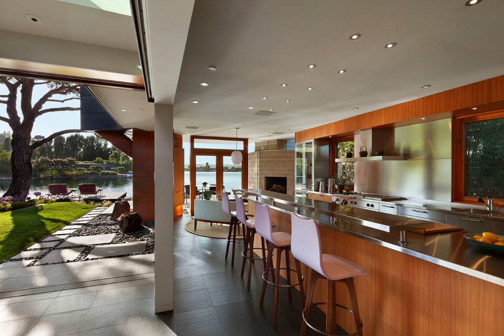 На фото: кухня в современном стиле с обеденным столом, плоскими фасадами, фартуком цвета металлик и техникой из нержавеющей стали с