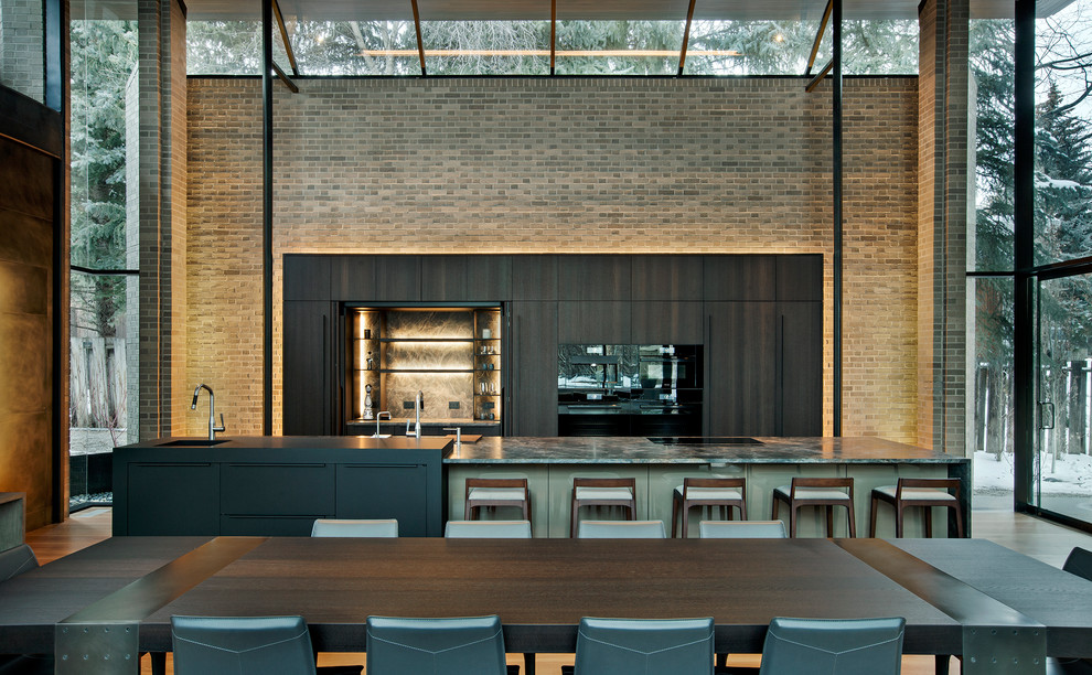Идея дизайна: параллельная кухня в современном стиле с обеденным столом, врезной мойкой, плоскими фасадами, темными деревянными фасадами, серым фартуком, черной техникой, паркетным полом среднего тона, островом, коричневым полом и серой столешницей