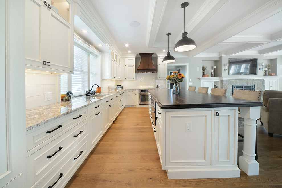 Example of a large arts and crafts l-shaped light wood floor and brown floor open concept kitchen design in Boston with an undermount sink, beaded inset cabinets, white cabinets, quartzite countertops, white backsplash, ceramic backsplash, stainless steel appliances and an island