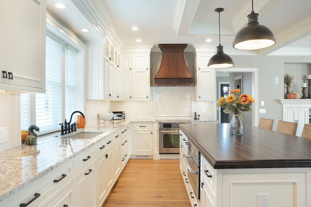 Exempel på ett stort klassiskt kök, med en undermonterad diskho, luckor med profilerade fronter, vita skåp, bänkskiva i kvartsit, vitt stänkskydd, stänkskydd i keramik, rostfria vitvaror, ljust trägolv, en köksö och brunt golv