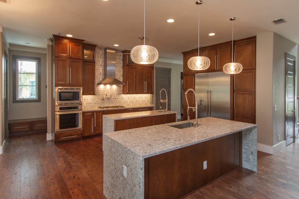 Inspiration for a large contemporary l-shaped medium tone wood floor open concept kitchen remodel in Orlando with an undermount sink, shaker cabinets, medium tone wood cabinets, granite countertops, white backsplash, ceramic backsplash, stainless steel appliances and two islands
