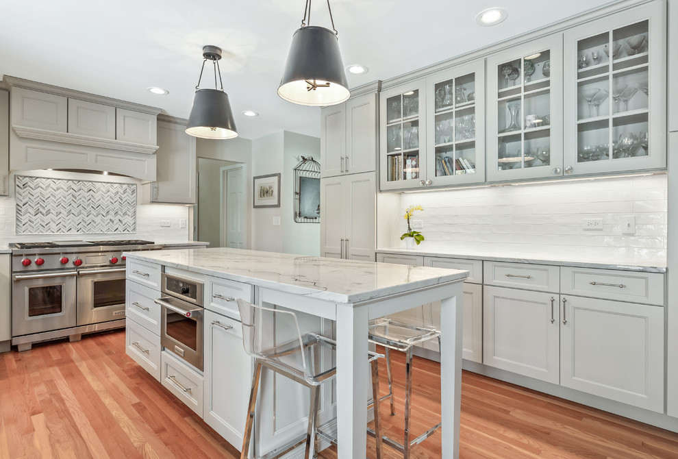 Inspiration for a large transitional u-shaped medium tone wood floor and brown floor eat-in kitchen remodel in Chicago with a single-bowl sink, shaker cabinets, gray cabinets, quartzite countertops, white backsplash, porcelain backsplash, stainless steel appliances, an island and gray countertops