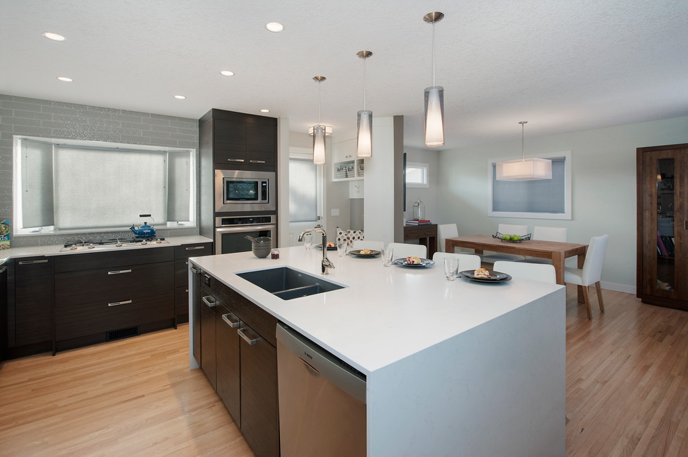 Inspiration for a huge contemporary l-shaped light wood floor eat-in kitchen remodel in Calgary with a double-bowl sink, flat-panel cabinets, dark wood cabinets, solid surface countertops, gray backsplash, glass tile backsplash, stainless steel appliances and an island