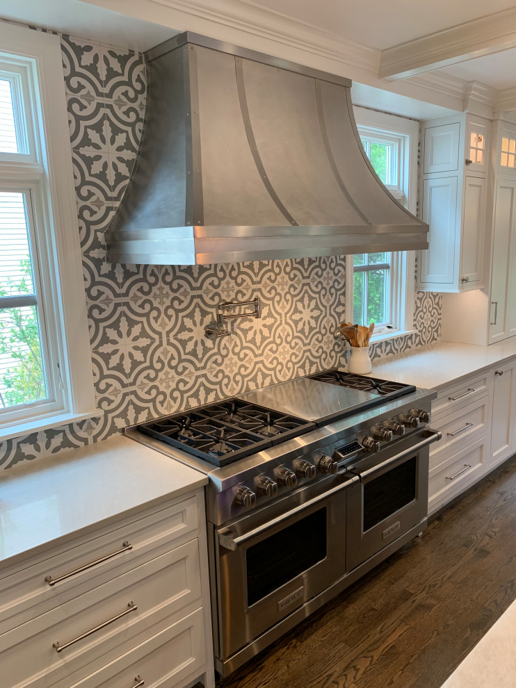 Large traditional l-shaped open plan kitchen in Chicago with recessed-panel cabinets, white cabinets, engineered stone countertops, cement tile splashback, stainless steel appliances, dark hardwood flooring, an island, brown floors and white worktops.
