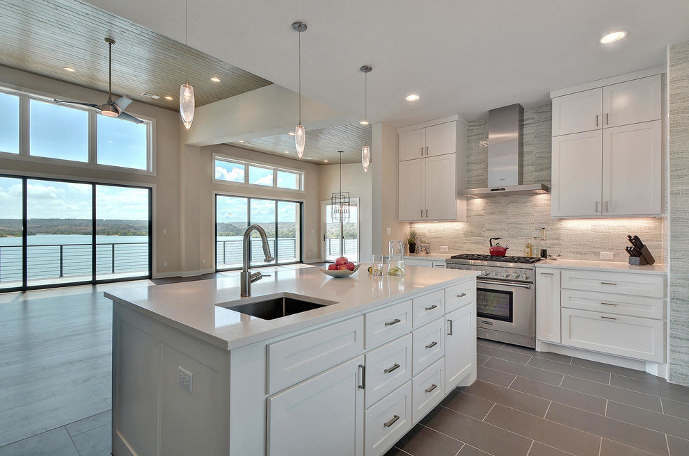 Example of a large trendy u-shaped porcelain tile and gray floor open concept kitchen design in Austin with an undermount sink, shaker cabinets, white cabinets, quartz countertops, stone tile backsplash, stainless steel appliances, an island and white backsplash