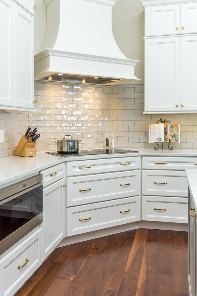 Bild på ett mellanstort vintage kök, med en undermonterad diskho, luckor med infälld panel, vita skåp, bänkskiva i kvarts, vitt stänkskydd, stänkskydd i keramik, rostfria vitvaror, mellanmörkt trägolv, en köksö och brunt golv