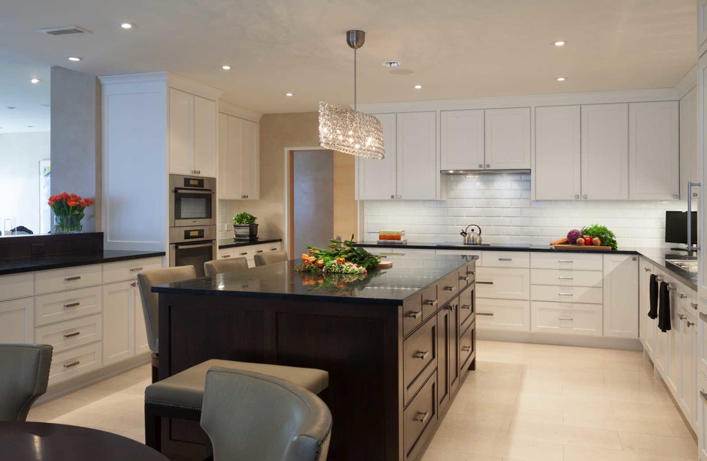 Photo of a large contemporary u-shaped open plan kitchen in Minneapolis with a built-in sink, recessed-panel cabinets, white cabinets, soapstone worktops, white splashback, metro tiled splashback, stainless steel appliances, limestone flooring, an island and beige floors.