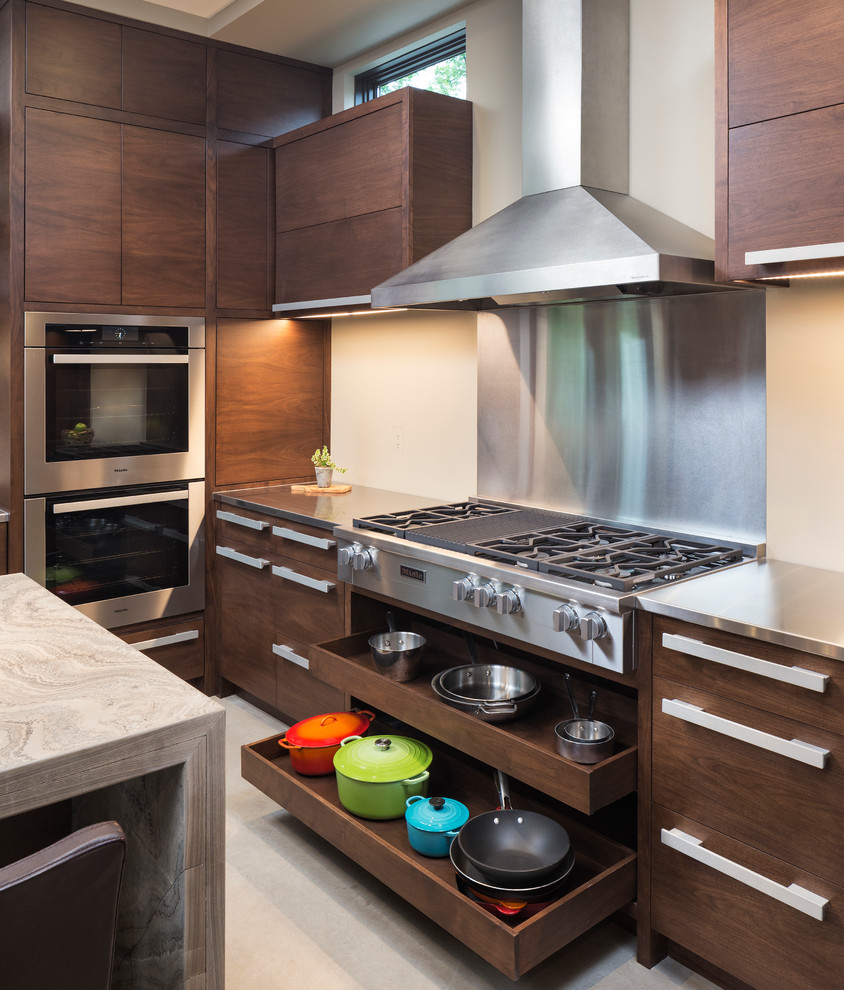 Cette photo montre une petite cuisine moderne en bois brun avec un placard à porte plane, un plan de travail en calcaire, une crédence beige, un électroménager en acier inoxydable, sol en béton ciré et îlot.