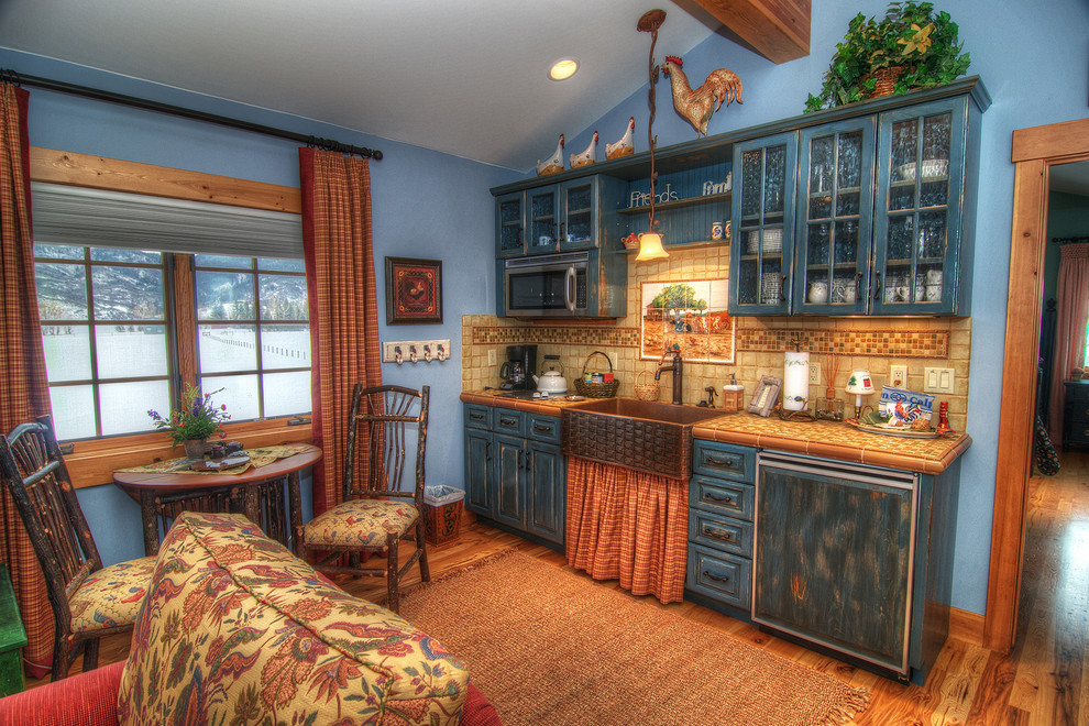 Bild på ett litet rustikt linjärt kök och matrum, med en rustik diskho, luckor med upphöjd panel, skåp i slitet trä, kaklad bänkskiva, flerfärgad stänkskydd, stänkskydd i stenkakel, färgglada vitvaror och mellanmörkt trägolv