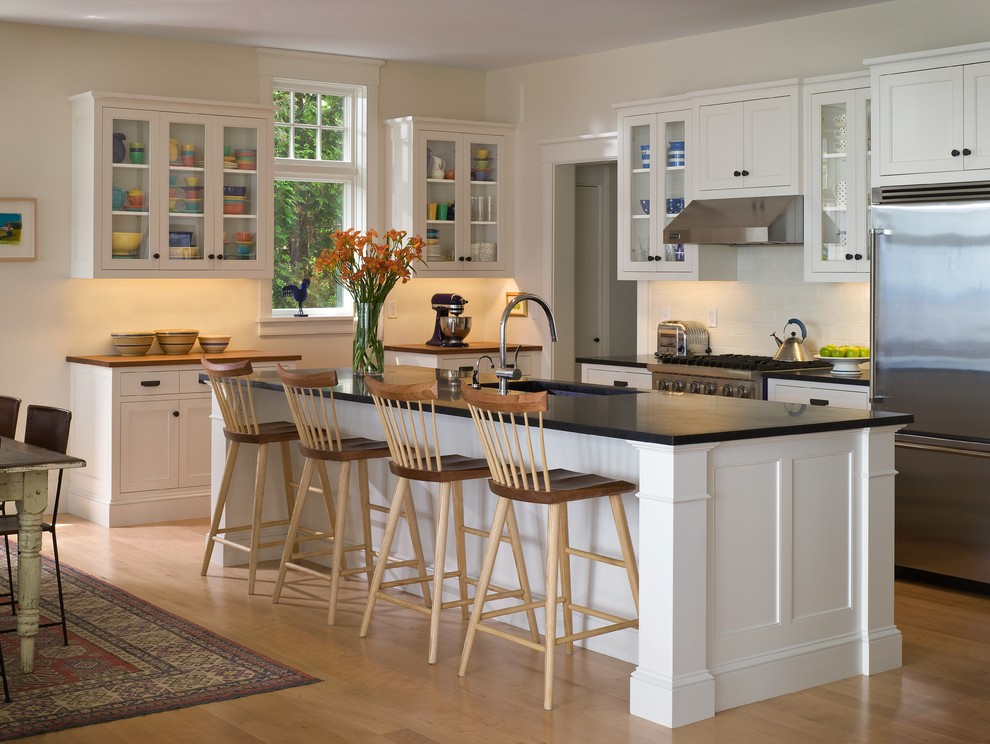 Immagine di una cucina vittoriana con lavello sottopiano, ante di vetro, ante bianche, paraspruzzi bianco, elettrodomestici in acciaio inossidabile e pavimento in legno massello medio