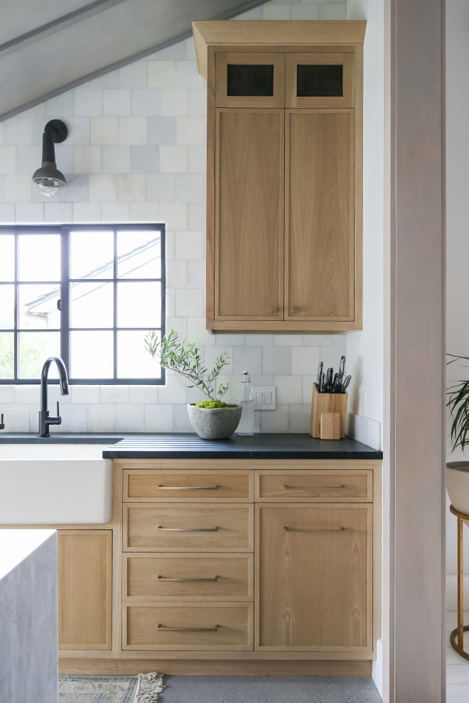 This is an example of a beach style kitchen/diner in Orange County with a belfast sink, light wood cabinets, marble worktops, marble splashback, stainless steel appliances, ceramic flooring, an island and grey floors.