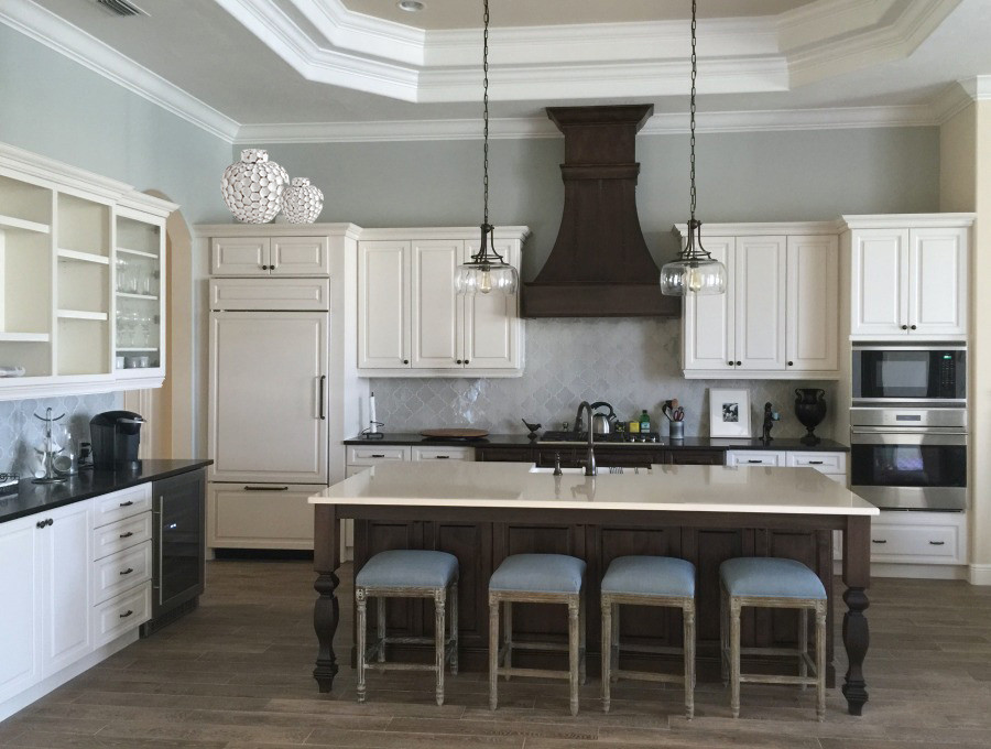 Inspiration for a mid-sized coastal l-shaped dark wood floor and brown floor eat-in kitchen remodel in Tampa with a farmhouse sink, raised-panel cabinets, white cabinets, quartzite countertops, gray backsplash, marble backsplash, stainless steel appliances and an island