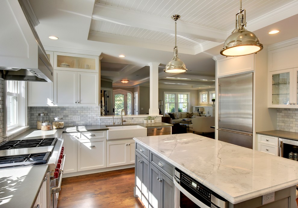 Example of a large beach style u-shaped medium tone wood floor and brown floor enclosed kitchen design in Phoenix with a farmhouse sink, recessed-panel cabinets, white cabinets, gray backsplash, marble backsplash, stainless steel appliances, an island and gray countertops