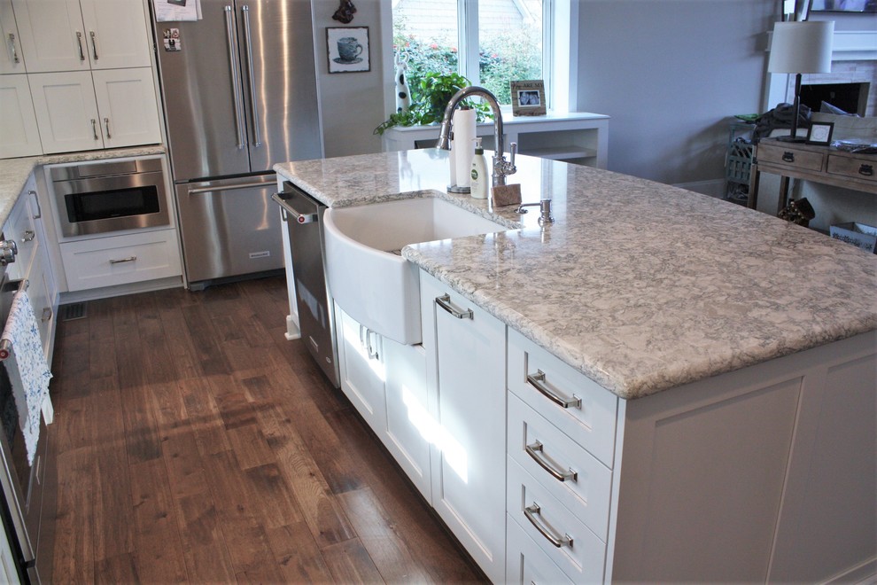 Coastal kitchen in Charlotte with a belfast sink, shaker cabinets, white cabinets, engineered stone countertops, white splashback, stone tiled splashback and dark hardwood flooring.