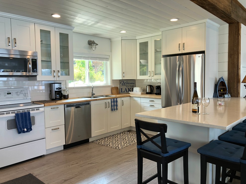 This is an example of a medium sized nautical u-shaped open plan kitchen in Other with a built-in sink, shaker cabinets, white cabinets, engineered stone countertops, white splashback, ceramic splashback, stainless steel appliances, laminate floors, a breakfast bar, grey floors and white worktops.