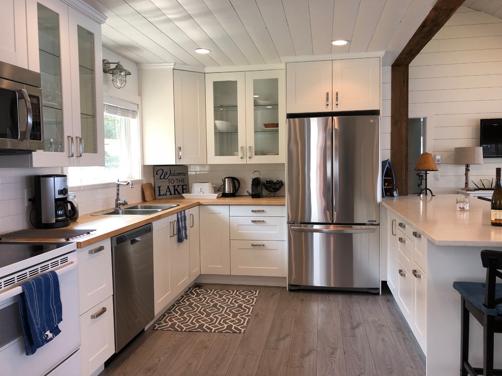 Photo of a medium sized nautical u-shaped open plan kitchen in Other with a built-in sink, shaker cabinets, white cabinets, engineered stone countertops, white splashback, ceramic splashback, stainless steel appliances, laminate floors, a breakfast bar, grey floors and white worktops.
