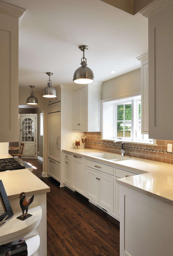 This is an example of a classic galley kitchen in Minneapolis with a submerged sink, shaker cabinets, white cabinets, brown splashback, metro tiled splashback and integrated appliances.