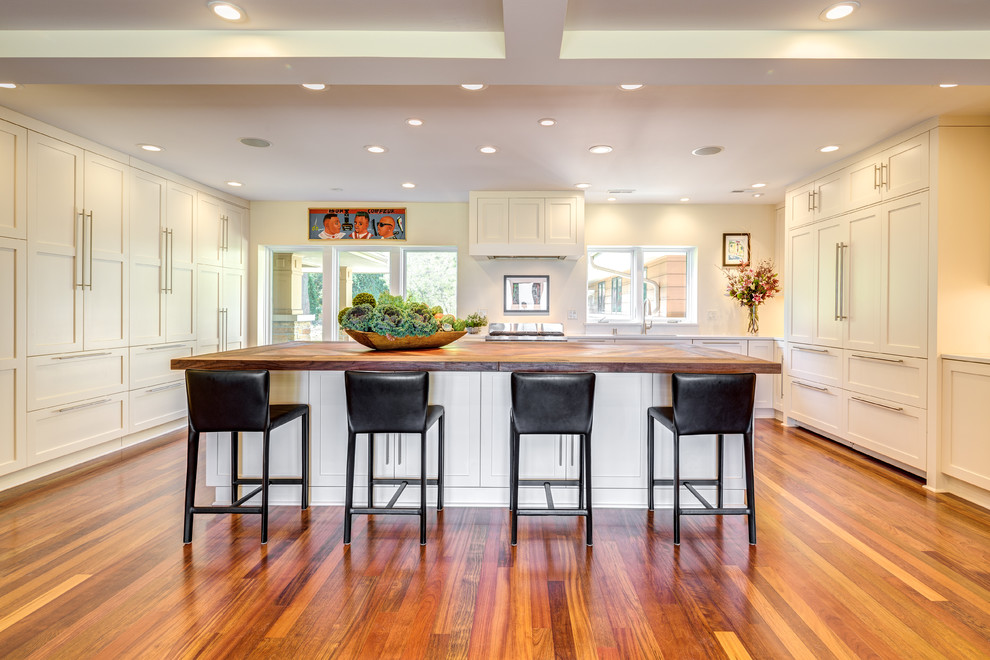 Modern inredning av ett stort brun brunt kök, med en undermonterad diskho, luckor med infälld panel, vita skåp, träbänkskiva, rostfria vitvaror, mellanmörkt trägolv, en köksö och brunt golv
