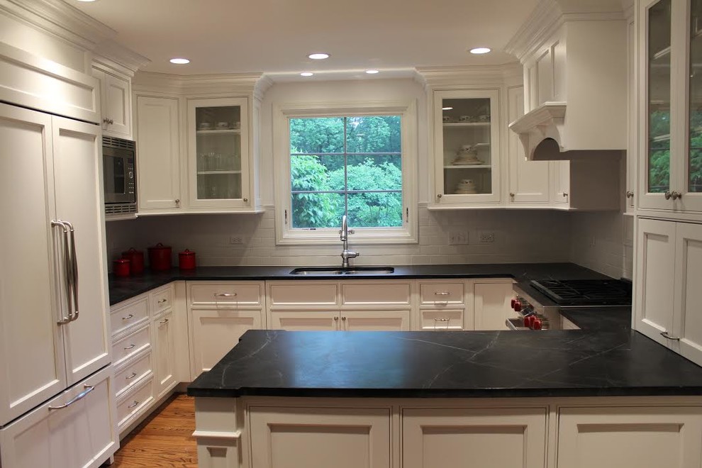 Enclosed kitchen - mid-sized traditional u-shaped medium tone wood floor enclosed kitchen idea in Chicago with a double-bowl sink, beaded inset cabinets, white cabinets, soapstone countertops, white backsplash, subway tile backsplash, stainless steel appliances and a peninsula