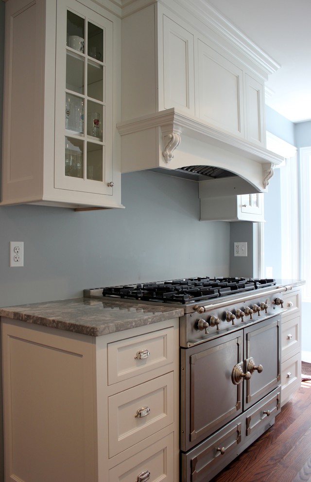 This is an example of a medium sized traditional u-shaped open plan kitchen in Chicago with a belfast sink, recessed-panel cabinets, white cabinets, stainless steel appliances, dark hardwood flooring, quartz worktops, a breakfast bar, brown floors and grey worktops.