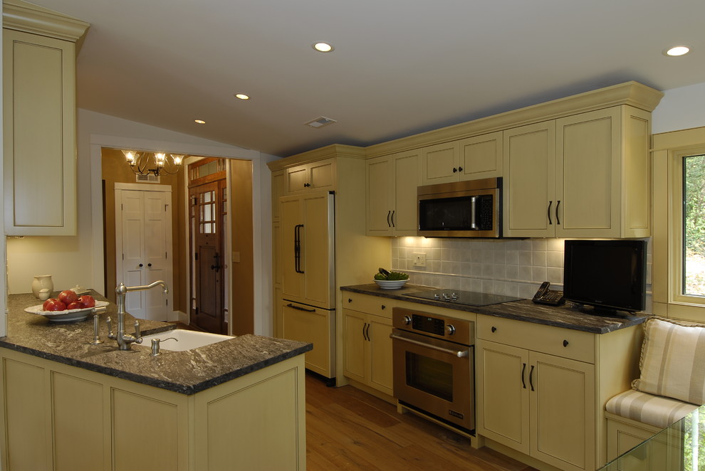 Inspiration for a small classic galley kitchen/diner in New York with a belfast sink, recessed-panel cabinets, yellow cabinets, granite worktops, beige splashback, porcelain splashback, stainless steel appliances and light hardwood flooring.