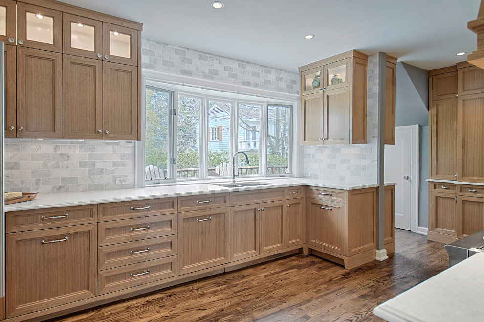 This is an example of a medium sized classic u-shaped kitchen in Milwaukee with a submerged sink, recessed-panel cabinets, medium wood cabinets, engineered stone countertops, grey splashback, marble splashback, integrated appliances, medium hardwood flooring, no island, brown floors and white worktops.