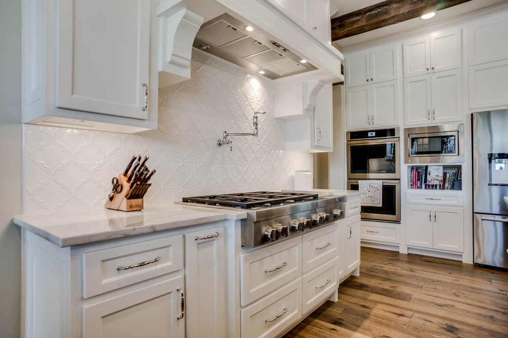 Bild på ett stort vintage vit vitt kök, med en rustik diskho, skåp i shakerstil, bruna skåp, bänkskiva i kvartsit, vitt stänkskydd, stänkskydd i keramik, rostfria vitvaror, mellanmörkt trägolv, en köksö och brunt golv