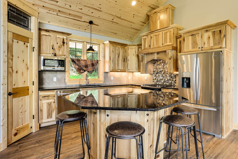 Photo of a rustic l-shaped kitchen in Minneapolis with a submerged sink, shaker cabinets, light wood cabinets, beige splashback, stainless steel appliances, medium hardwood flooring, an island and black worktops.