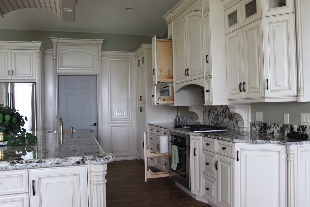 Mid-sized elegant l-shaped medium tone wood floor and brown floor enclosed kitchen photo in Other with an undermount sink, raised-panel cabinets, white cabinets, granite countertops, multicolored backsplash, stone slab backsplash, stainless steel appliances and an island