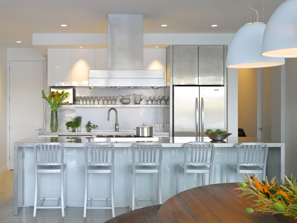 Imagen de cocina comedor contemporánea con una isla, armarios con paneles lisos, puertas de armario blancas, encimera de acero inoxidable, salpicadero blanco, electrodomésticos de acero inoxidable y suelo de cemento