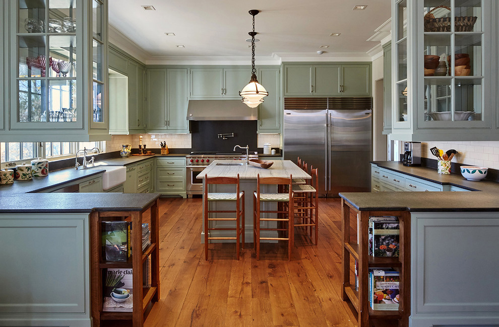 Klassische Küche in U-Form mit Schrankfronten im Shaker-Stil, grünen Schränken, Küchenrückwand in Weiß, Rückwand aus Metrofliesen, braunem Holzboden, Kücheninsel und Landhausspüle in New York