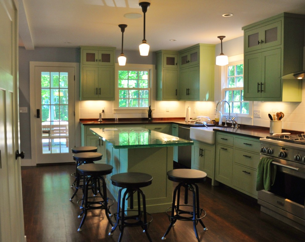 Inredning av ett klassiskt mellanstort kök, med en rustik diskho, luckor med infälld panel, gröna skåp, stänkskydd i tunnelbanekakel, rostfria vitvaror, en köksö, bänkskiva i glas, vitt stänkskydd och mörkt trägolv