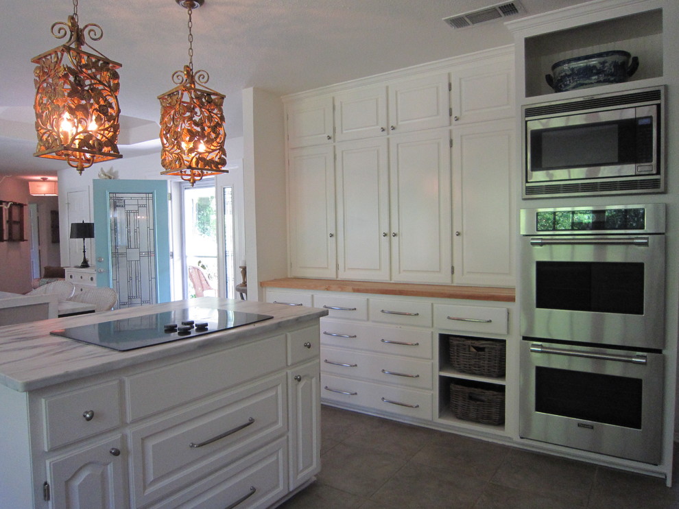Offene Stilmix Küche in L-Form mit Landhausspüle, profilierten Schrankfronten, weißen Schränken, Arbeitsplatte aus Holz, Küchengeräten aus Edelstahl, Porzellan-Bodenfliesen und Kücheninsel in Dallas