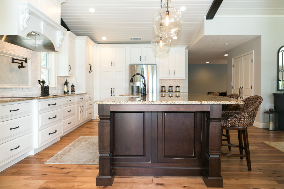 Large elegant light wood floor and brown floor eat-in kitchen photo in Orlando with a farmhouse sink, recessed-panel cabinets, white cabinets, granite countertops, white backsplash, stone tile backsplash, stainless steel appliances and an island