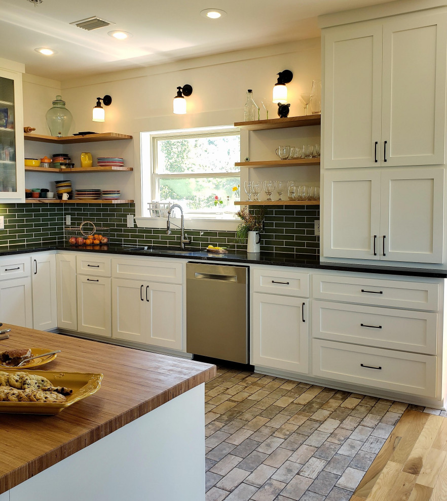 Inspiration for a medium sized traditional u-shaped kitchen/diner in Little Rock with a single-bowl sink, flat-panel cabinets, white cabinets, granite worktops, green splashback, ceramic splashback, stainless steel appliances, brick flooring, a breakfast bar, grey floors and black worktops.