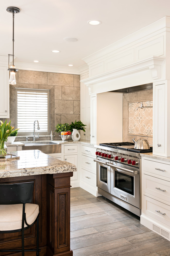 Klassisk inredning av ett mellanstort brun brunt kök, med en rustik diskho, vita skåp, granitbänkskiva, brunt stänkskydd, integrerade vitvaror, mellanmörkt trägolv, en köksö, brunt golv, stänkskydd i porslinskakel och luckor med profilerade fronter