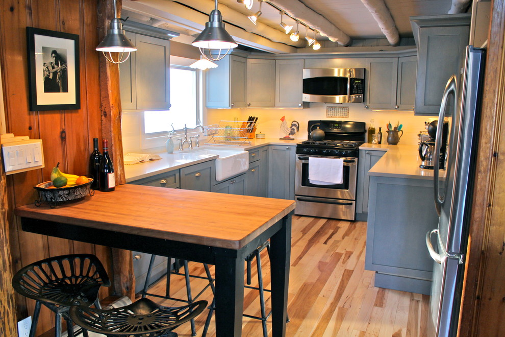 Foto på ett rustikt kök, med en rustik diskho, luckor med infälld panel, blå skåp, bänkskiva i kvarts, vitt stänkskydd, stänkskydd i keramik, rostfria vitvaror och ljust trägolv